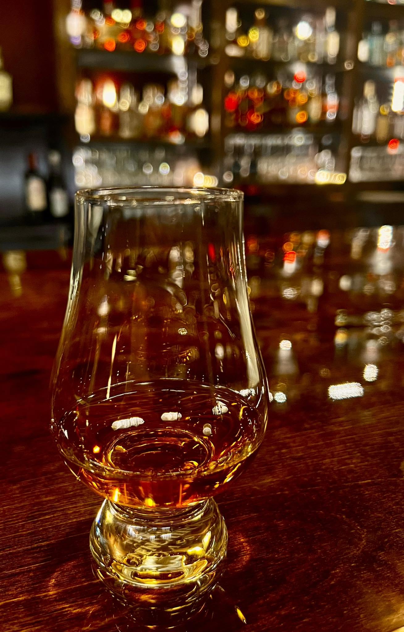 A tasting glass of whiskey on the bar, the back bar softly out of focus